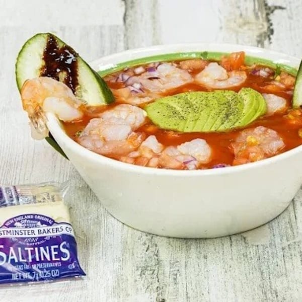 Shrimp cocktail with avocado, cucumber, and red sauce, served with a packet of saltines.