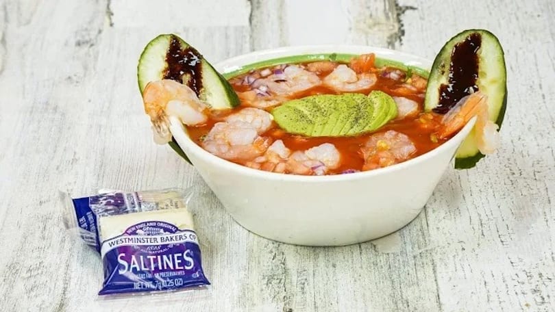 Shrimp cocktail with avocado, cucumber, and red sauce, served with a packet of saltines.