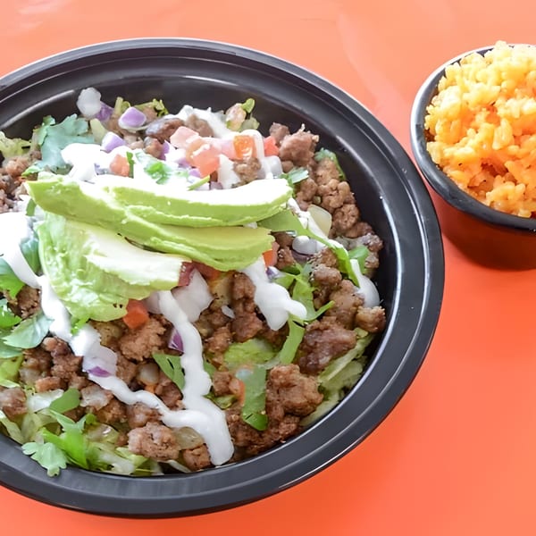 Taco salad bowl with ground beef, lettuce, avocado, and sour cream, with a side of rice.
