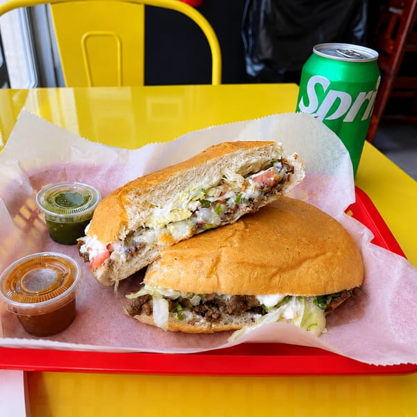 A torta sandwich, cut in half, with two sauces and a Sprite on a yellow table.