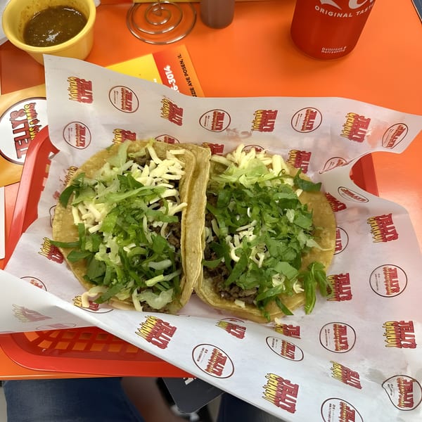 Two tacos with meat, cheese, and lettuce on branded paper, with salsa and a Coca-Cola.