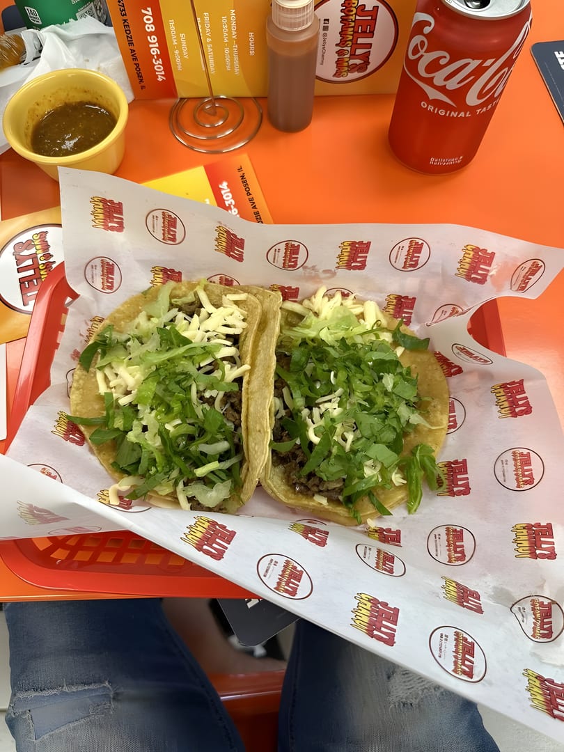Two tacos with meat, cheese, and lettuce on branded paper, with salsa and a Coca-Cola.